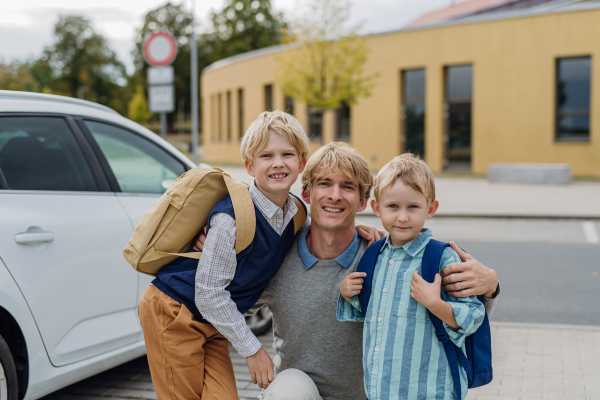 Father saying goodbyeto to his sons in front of school building. Dad heading to work. Concept of work-life balance for parents.