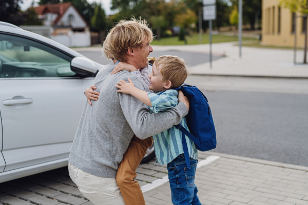 Father saying goodbye to sons in front of school building, hugging both boys. Dad heading to work. Concept of work-life balance for parents.