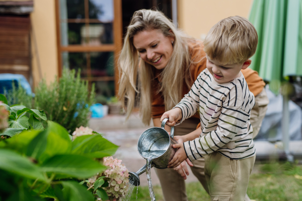 Mother and little son taking care of plants in the garden, replanting, watering flowers. Mom and boy spending quality time together, bonding.