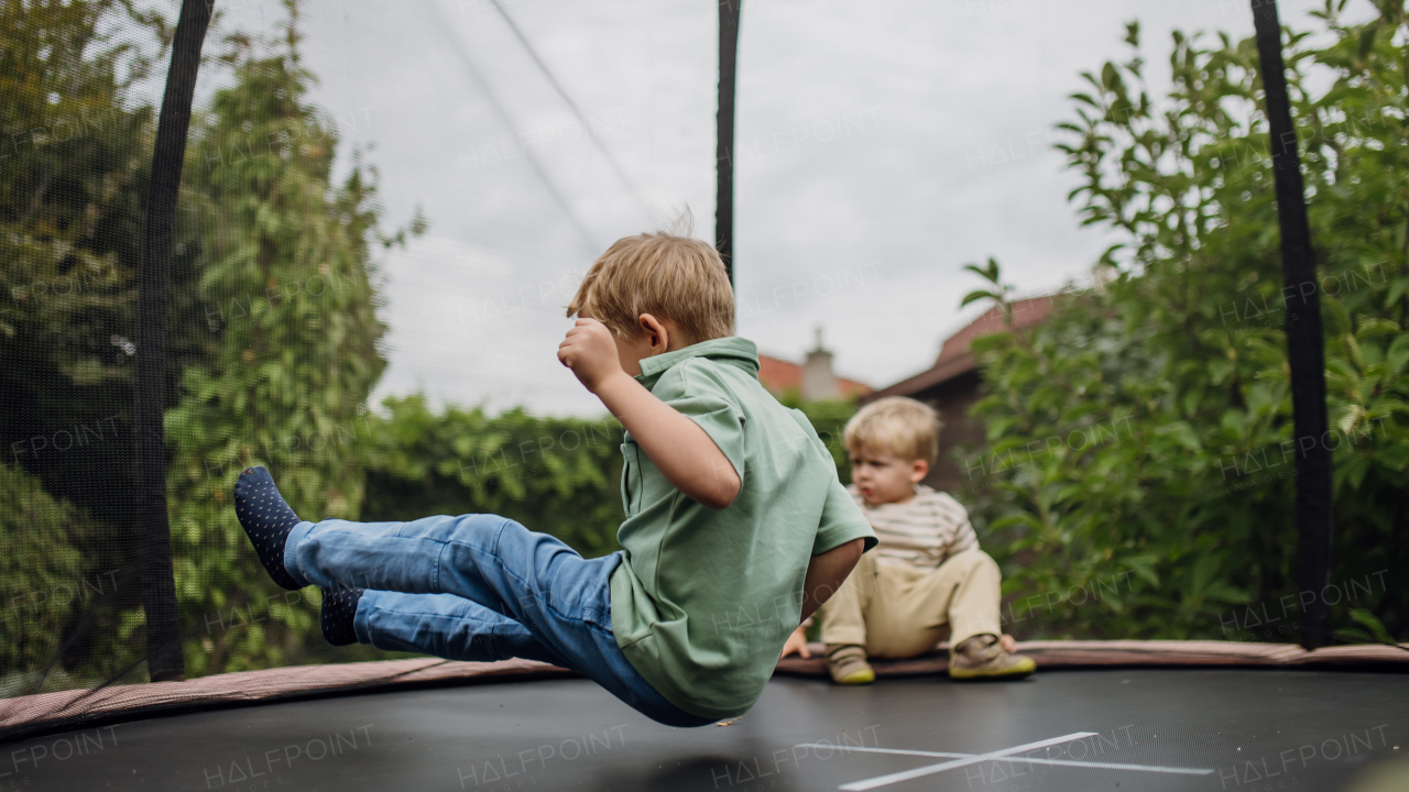 Little boys, brothers jumping on trampoline in the backyard, doing somersaults. Dangers and risks of trampoline for the kids.