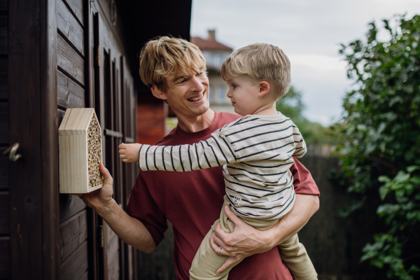 Father with little son making an bug hotel, or insect house outdoors in the garden. Boy learning about insects, garden ecosystem and biodiversity.