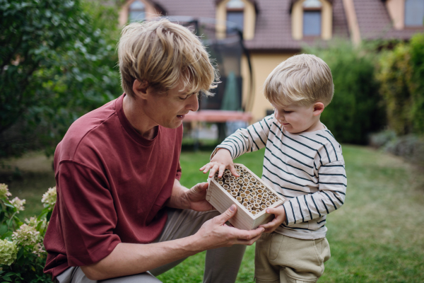 Father with little son making an bug hotel, or insect house outdoors in the garden. Boy learning about insects, garden ecosystem and biodiversity.