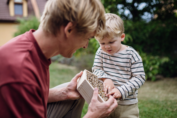 Father with little son making an bug hotel, or insect house outdoors in the garden. Boy learning about insects, garden ecosystem and biodiversity.