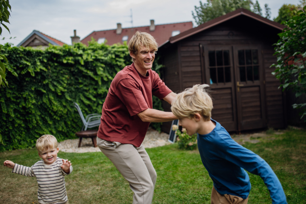 Father having fun with sons in the garden, chasing each other having bonding moment. Concept of Father's Day, and fatherly love.