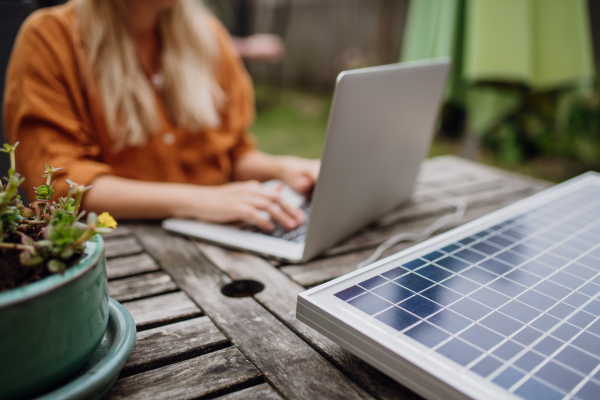 Businesswoman, freelancer or manager working outdoors in the garden, garden homeoffice. Remote work from backyard. Laptop is charging with solar charger. Concept of working remotely.