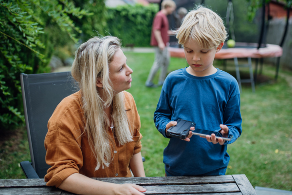 Mother explaining son how solar energy working, how to charge smartphone with solar charger. Concept of sustainability and green energy.