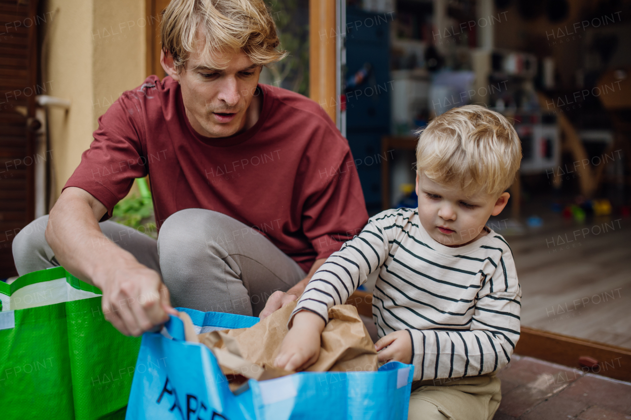 Father teaching son recycle waste. Boy sorting the waste according to material into colored bags. Concept of sustainable family.