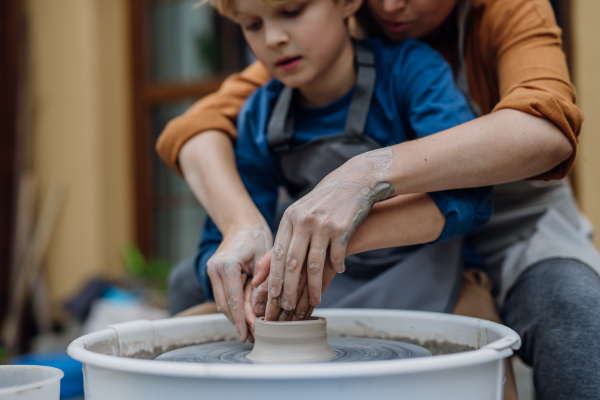 Mother teaching son how to make pottery on pottery wheel. Child creative activities and art. Boy making pottery, having fun with mom. Happy family moment.