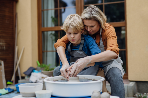 Mother teaching son how to make pottery on pottery wheel. Child creative activities and art. Boy making pottery, having fun with mom. Happy family moment.