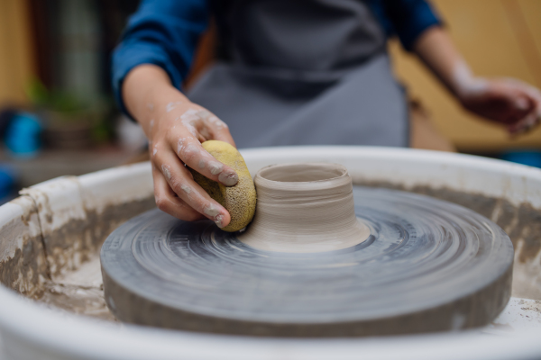 Close up woman making pottery on pottery wheel. Child creative activities and art. Boy making pottery with mom, having fun. Happy family moment.