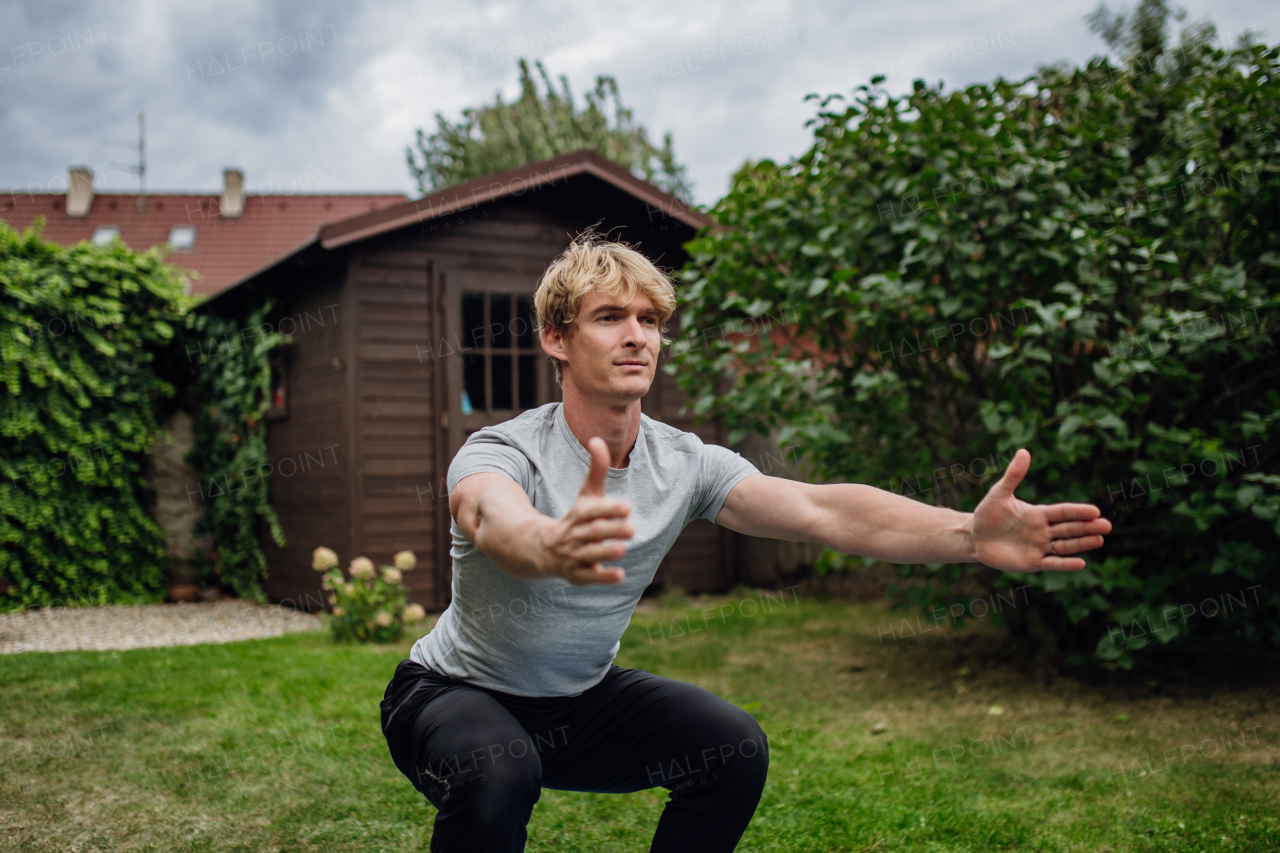 Middle aged man stretching, exercising outdoors in garden, squatting. Concept of workout routine at home.