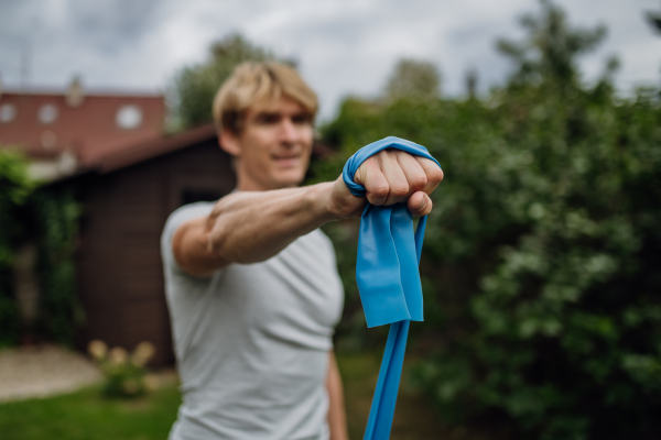 Middle aged man doing strength exercises with resistance band outdoors in the garden. Concept of workout routine at home.