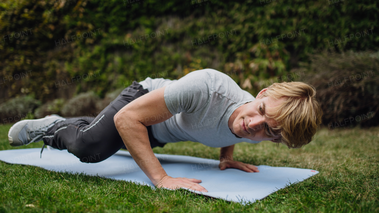 Middle aged man stretching, exercising outdoors in garden, push ups. Concept of workout routine at home.