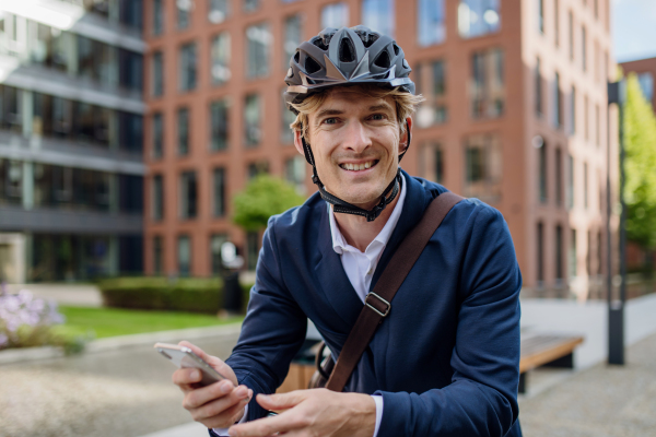 Handsome middle-aged man commuting through the city by bike in black suit, holding smartphone. Male city commuter traveling from work by bike after a long workday.