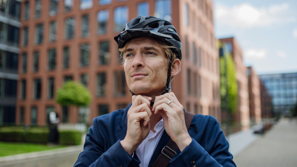 Handsome middle-aged man commuting through the city by bike, fastening helmet on head. Male city commuter traveling from work by bike after a long workday.