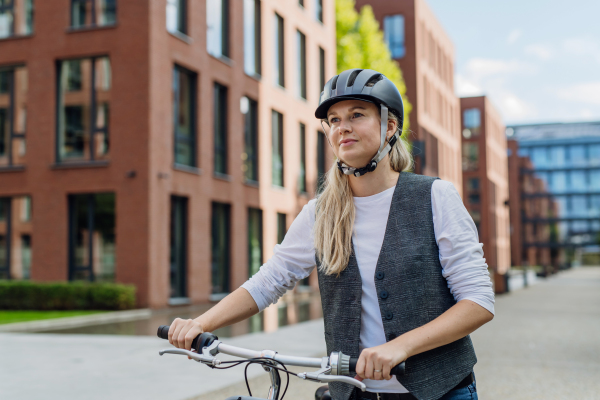 Beautiful middle-aged woman commuting through the city by bike. Female city commuter traveling from work by bike after a long workday.