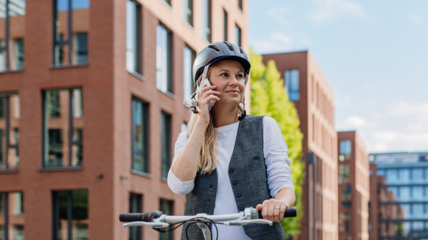 Beautiful middle-aged woman commuting through the city by bike, phone calling on smartphone. Female city commuter traveling from work by bike after a long workday.