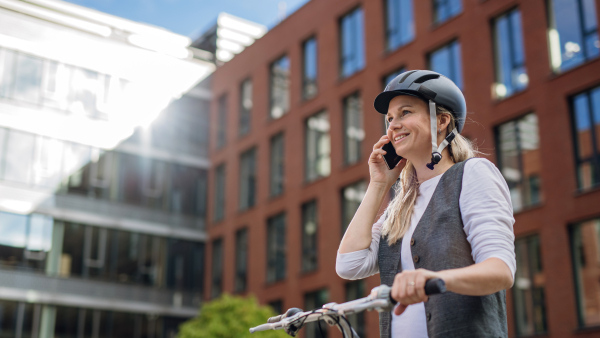 Beautiful middle-aged woman commuting through the city by bike, phone calling on smartphone. Female city commuter traveling from work by bike after a long workday.