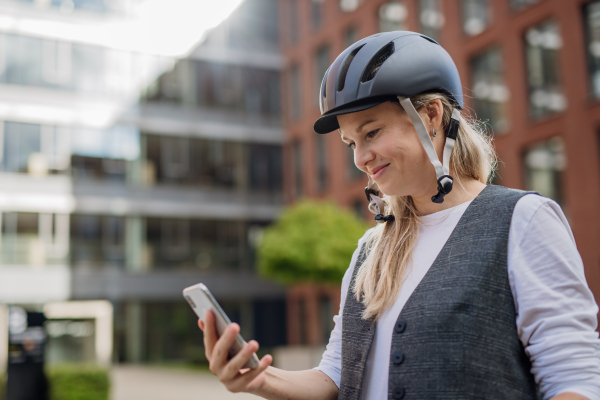 Beautiful middle-aged woman commuting through the city by bike, holding smartphone. Female city commuter traveling from work by bike after a long workday.