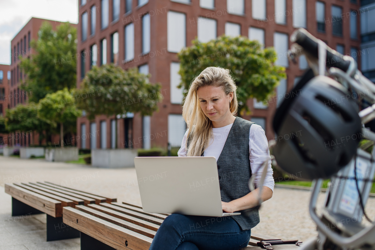 Portrait of businesswoman, freelancer or manager working outdoors in city park. Woman with laptop on knees, sitting on park bench during sunny day. Concept of working remotely.