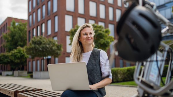 Portrait of businesswoman, freelancer or manager working outdoors in city park. Woman with laptop on knees sitting on park bench during sunny day. Concept of working remotely.