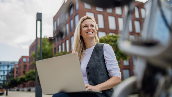 Portrait of businesswoman, freelancer or manager working outdoors in city park. Woman with laptop on knees making call on smartphone, sitting on park bench during sunny day. Concept of working remotely.