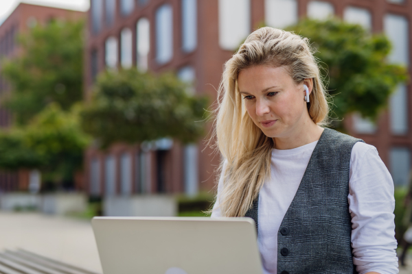 Portrait of businesswoman, freelancer or manager working outdoors in city park. Woman with laptop on knees sitting on park bench during sunny day. Concept of working remotely.