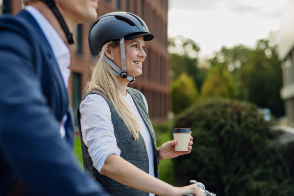 Beautiful middle-aged woman commuting through the city, buying, drinking coffe in front of office. Female city commuter with helmet traveling from work by bike after a long workday.