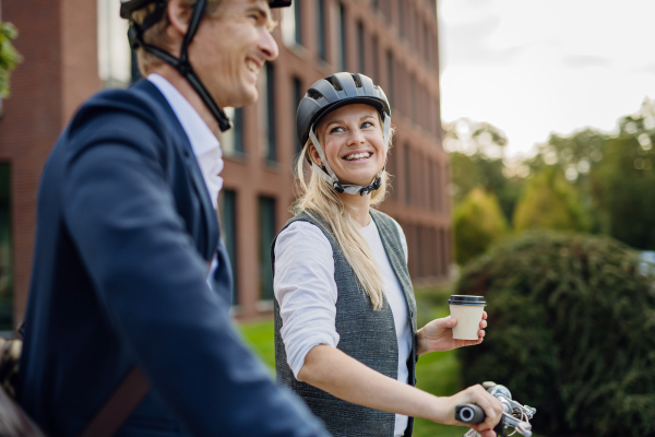 Spouses commuting through the city, talking and walking by bike on street. Middle-aged city commuters traveling from work by bike after a long workday. Husband and wife riding bikes in city.