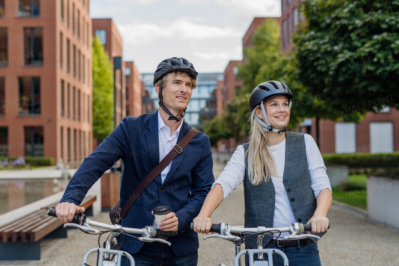 Spouses commuting through the city, talking and walking by bike on street. Middle-aged city commuters traveling from work by bike after a long workday. Husband and wife riding bikes in city.