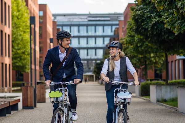 Spouses commuting through the city, riding bike on street. Middle-aged city commuters traveling from work by bike after a long workday. Husband and wife riding bikes in city.