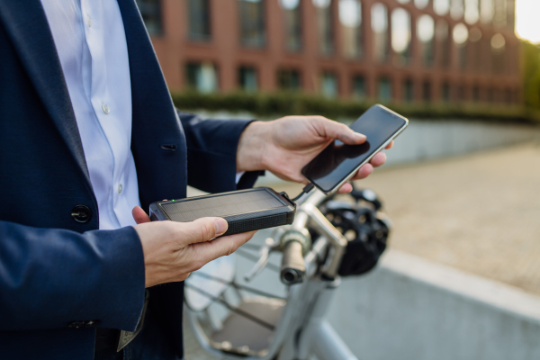 Portrait of businessman, freelancer or manager working outdoors in city park. Charging his smartphone with solar phone charger. Concept of working remotely.