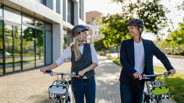 Spouses commuting through the city, talking and walking by bike on street. Middle-aged city commuters traveling from work by bike after a long workday. Husband and wife riding bikes in city.