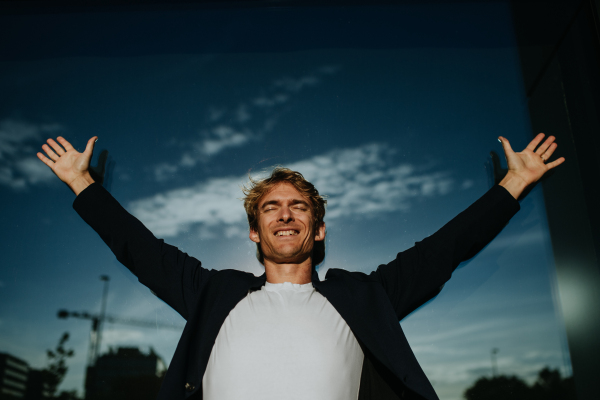 Portrait of handsome mature man with blond hair and closed eyes, standing outdoors in the city, in front of reflective wall.