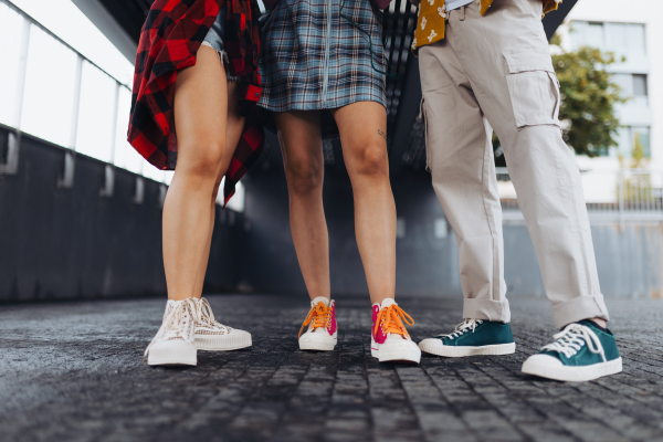 Close-up of young students' legs standing in the city. Zoomers in trendy stylish clothes standing in front of university building.