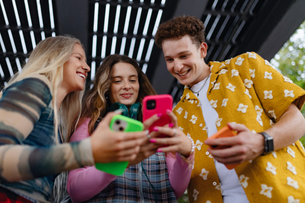 Generation z students hanging out together outdoors in the city. Young stylish zoomers are online, using smartphones, social media, taking selfies. Concept of power of friendship and social strength of gen Z. Low angle shot with copy space.