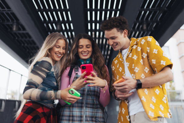 Generation z students hanging out together outdoors in the city. Young stylish zoomers are online, using smartphones, social media, taking selfies. Concept of power of friendship and social strength of gen Z. Low angle shot with copy space.