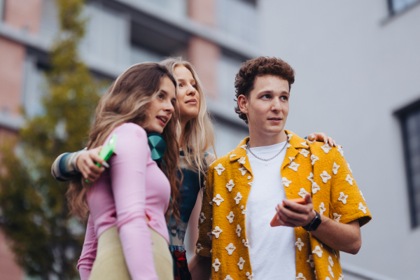 Generation z students hanging out together outdoors in the city. Young stylish zoomers are online, using smartphones, social media, taking selfies. Concept of power of friendship and social strength of gen Z.