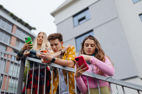 Generation z students hanging out together outdoors in the city. Young stylish zoomers are online, using smartphones, social media, taking selfies. Concept of power of friendship and social strength of gen Z.