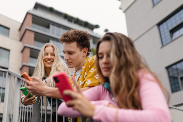 Generation z students hanging out together outdoors in the city. Young stylish zoomers are online, using smartphones, social media, taking selfies. Concept of power of friendship and social strength of gen Z.