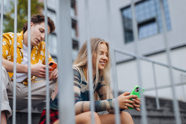 Couple sitting on concrete steps, each scrolling on their own smartphone. Together in person, but alone online.