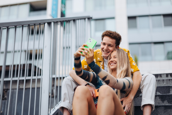 Portrait of generation z couple sitting outdoors in the city and taking selfie. Students spending free time online, watching social media content. Concept of gen Z as loneliest generation.