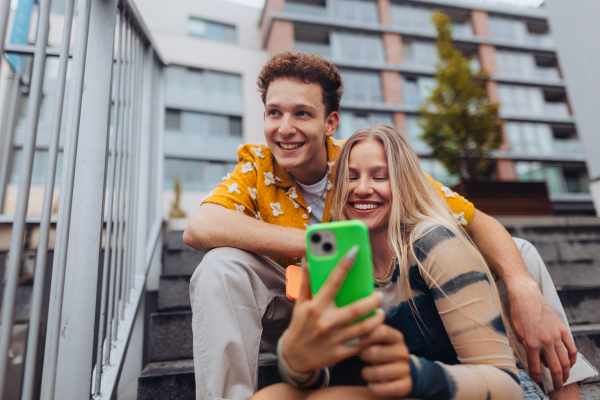 Portrait of generation z couple sitting outdoors in the city and taking selfie. Students spending free time online, watching social media content. Concept of gen Z as loneliest generation.