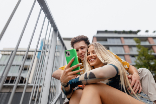 Portrait of generation z couple sitting outdoors in the city and taking selfie. Students spending free time online, watching social media content. Concept of gen Z as loneliest generation.