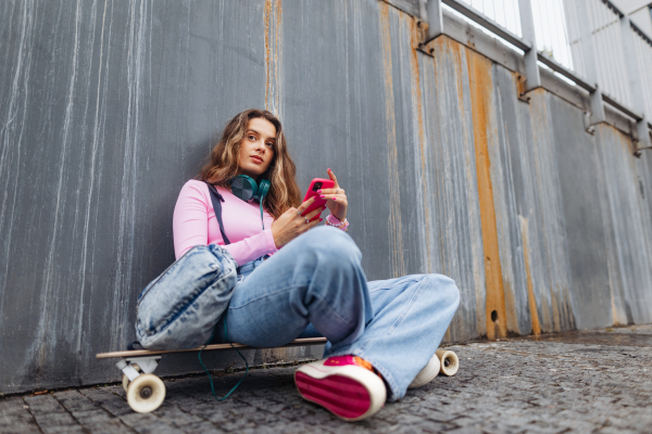 Portrait of generation z girl student sitting outdoors in the city. Student spending free time online and alone. Concept of gen Z as loneliest generation.