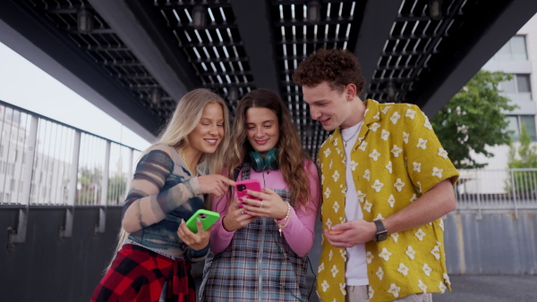 Generation z students hanging out together outdoors in the city. Young stylish zoomers are online, using smartphones, social media, taking selfies. Concept of power of friendship and social strength of gen Z. Low angle shot with copy space.