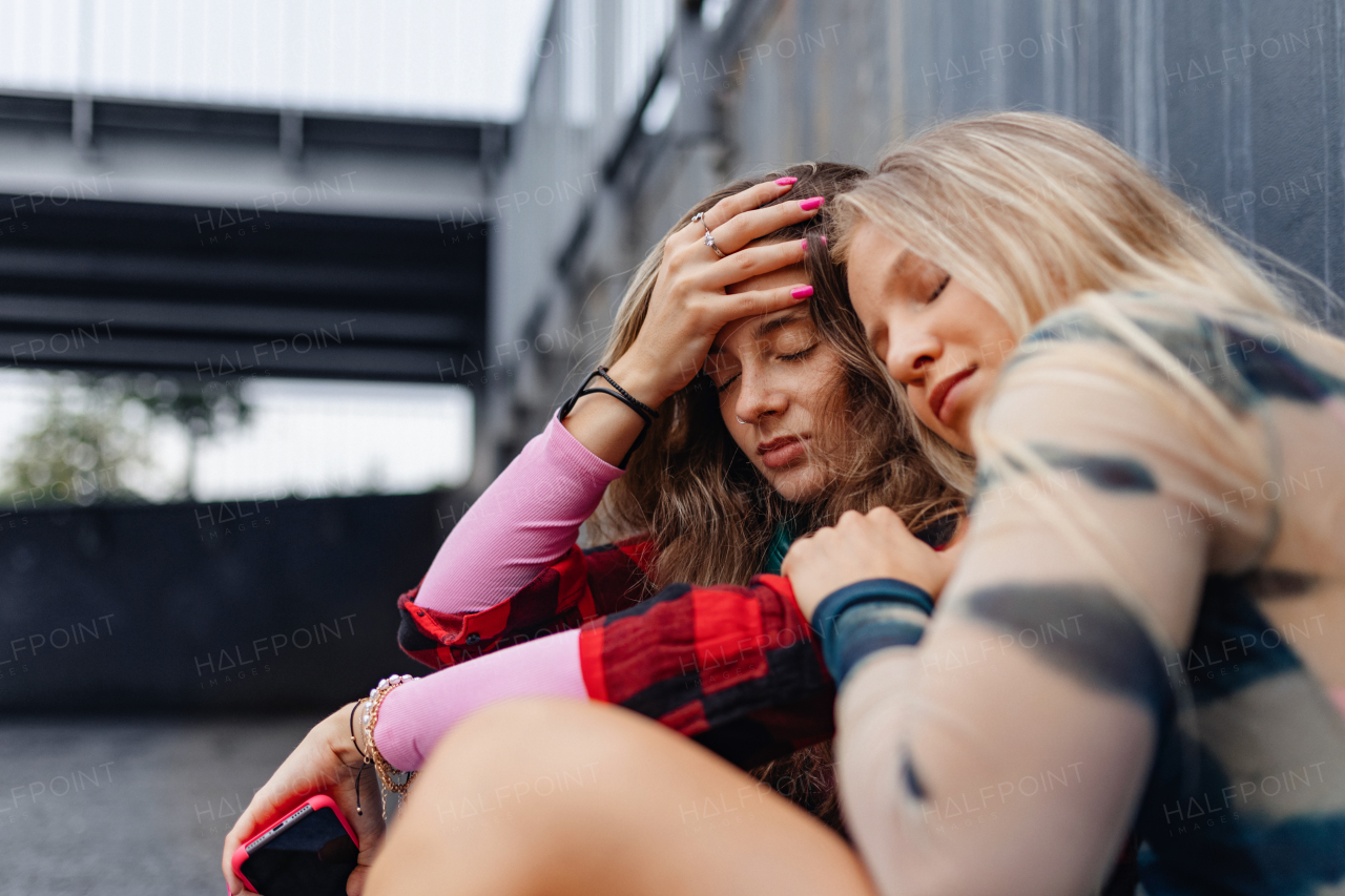 Gen Z friends sitting together outdoors in the city, comforting each other and helping with a problem. Anxiety and sadness of a young zoomer girl. Concept of power of friendship.