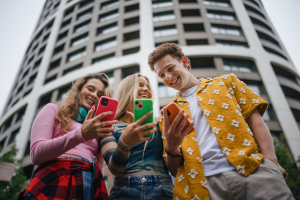 Generation z students hanging out together outdoors in the city. Young stylish zoomers are online, using smartphones, social media, taking selfies. Concept of power of friendship and social strength of gen Z. Low angle shot with copy space.