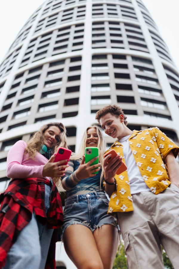 Generation z students hanging out together outdoors in the city. Young stylish zoomers are online, using smartphones, social media, taking selfies. Concept of power of friendship and social strength of gen Z. Low angle shot with copy space.