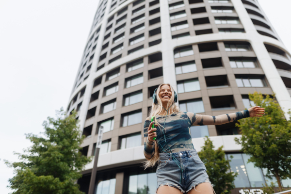 Portrait of a Generation Z girl student listening to music via headphones outdoors in the city. Student spending free time online and alone. Concept of gen Z as loneliest generation.